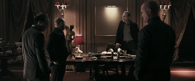 Wide shot frame from RocknRolla — standing, room, table