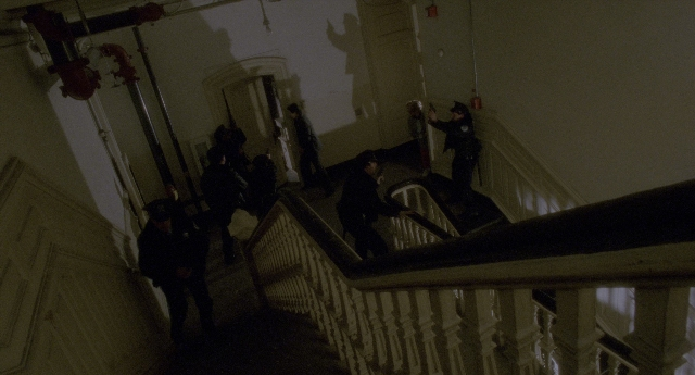 Wide shot frame from Twelve Monkeys — standing, room, fire