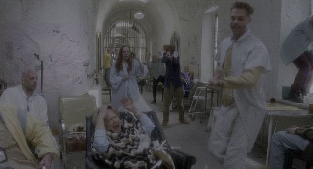 Wide shot frame from Twelve Monkeys — sitting, standing, room