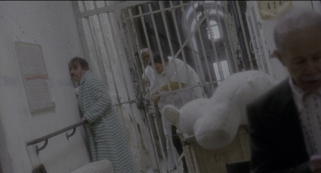 Wide shot frame from Twelve Monkeys — standing, coat, face