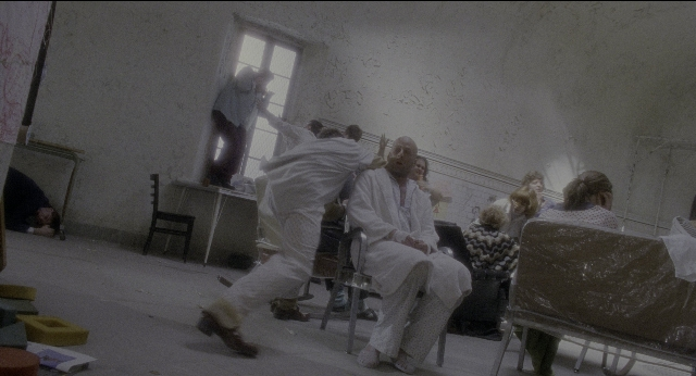 Wide shot frame from Twelve Monkeys — sitting, standing, room