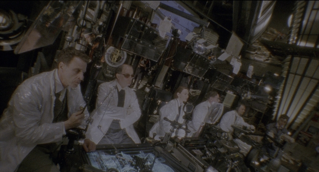 Wide shot frame from Twelve Monkeys — room, table, dialogue