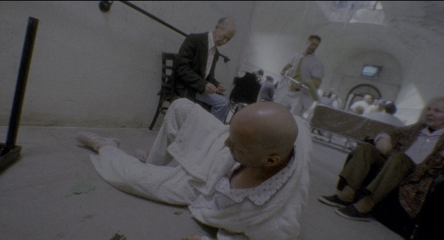 Wide shot frame from Twelve Monkeys — sitting, standing, room