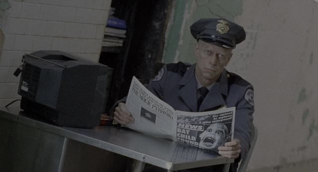 Wide shot frame from Twelve Monkeys — sitting, room, hat