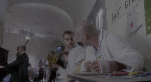 Wide shot frame from Twelve Monkeys — sitting, book, standing
