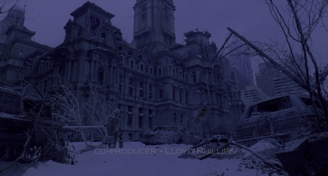 Wide shot frame from Twelve Monkeys — clock, snow, building