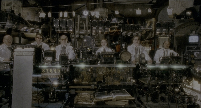 Wide shot frame from Twelve Monkeys — sitting, room, table
