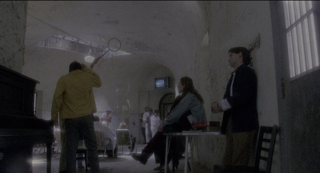 Wide shot frame from Twelve Monkeys — sitting, standing, room