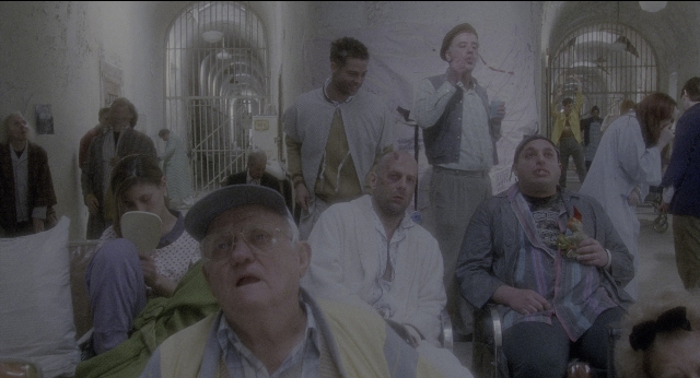 Wide shot frame from Twelve Monkeys — standing, room, hat