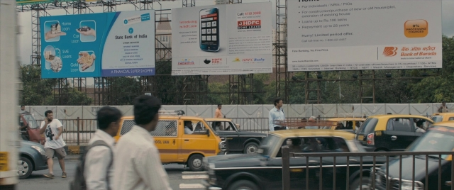Wide shot frame from The Lunchbox — walking, phone, street