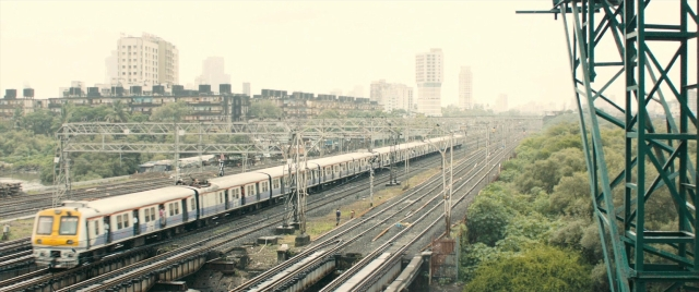Wide shot frame from The Lunchbox — skyscraper, train, running