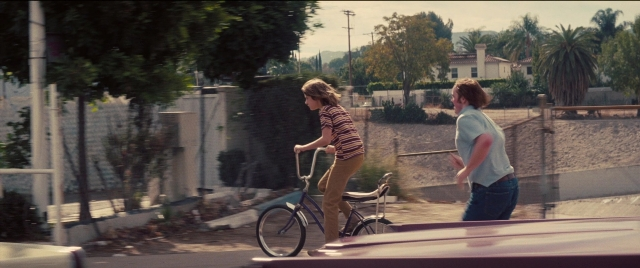 Wide shot frame from Licorice Pizza — dialogue, street, car