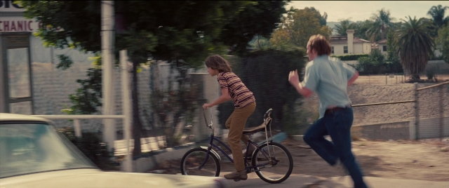 Wide shot frame from Licorice Pizza — street, car, bicycle