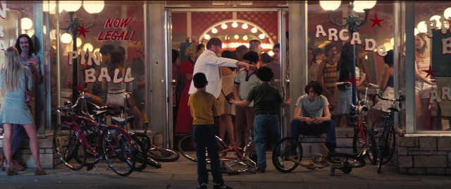 Wide shot frame from Licorice Pizza — sitting, standing, dialogue