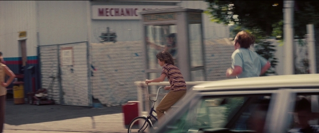 Wide shot frame from Licorice Pizza — phone, street, car