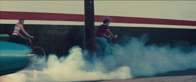 Wide shot frame from Licorice Pizza — street, car, bicycle