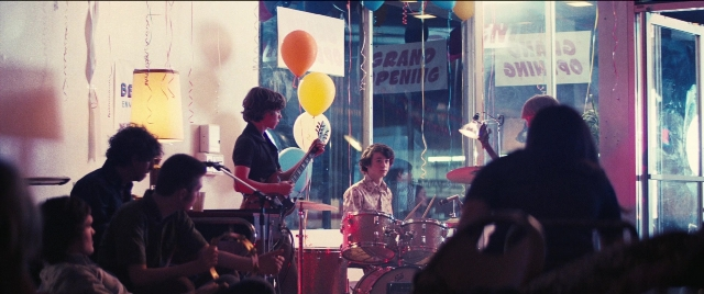 Wide shot frame from Licorice Pizza — sitting, standing, room