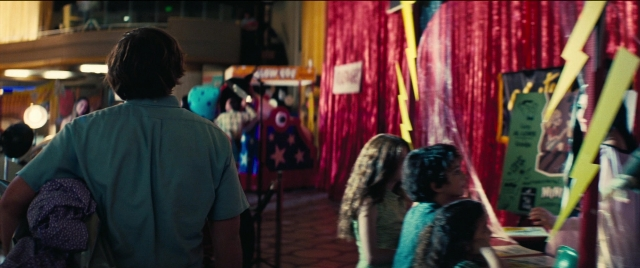 Wide shot frame from Licorice Pizza — standing, room, table