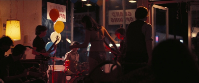 Wide shot frame from Licorice Pizza — sitting, standing, room