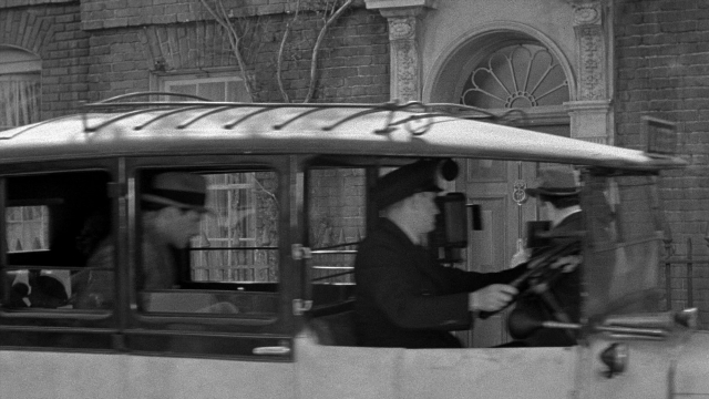 Wide shot frame from Foreign Correspondent — street, hat, car
