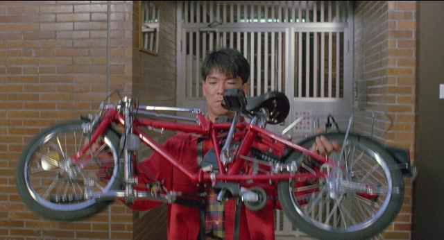 Wide shot frame from Fei lung mang jeung — standing, bicycle, bag