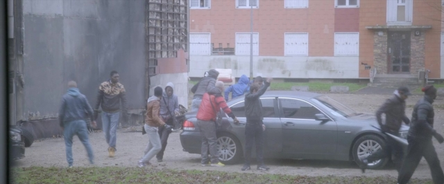 Wide shot frame from Dheepan — street, car, wheel
