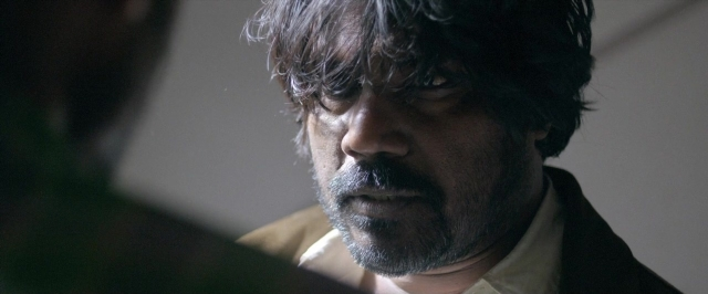 Wide shot frame from Dheepan — room, suit, tie