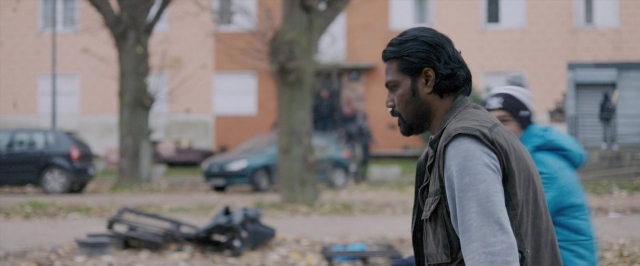 Wide shot frame from Dheepan — standing, street, car