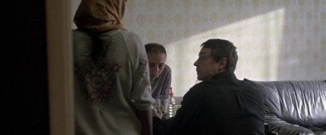 Wide shot frame from Dheepan — sitting, standing, room