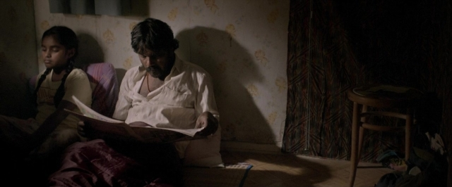 Wide shot frame from Dheepan — sitting, book, room