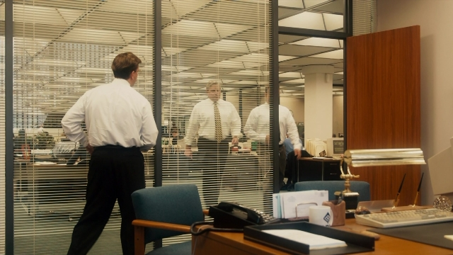 Wide shot frame from The Informant! — sitting, desk, standing