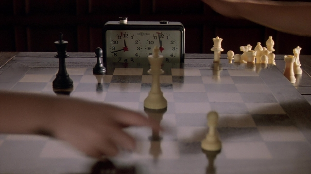 Wide shot frame from Searching for Bobby Fischer — table, hand, clock