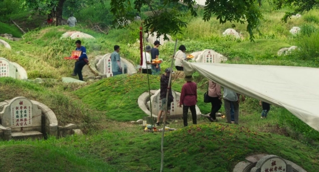 Wide shot frame from Lahn Mah — sitting, standing, tent