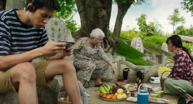 Wide shot frame from Lahn Mah — sitting, phone, dress
