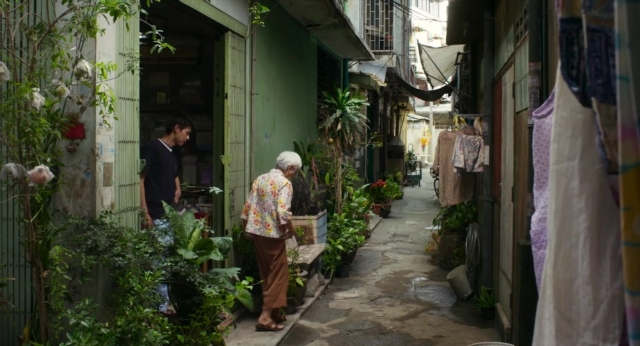 Wide shot frame from Lahn Mah — standing, door, street