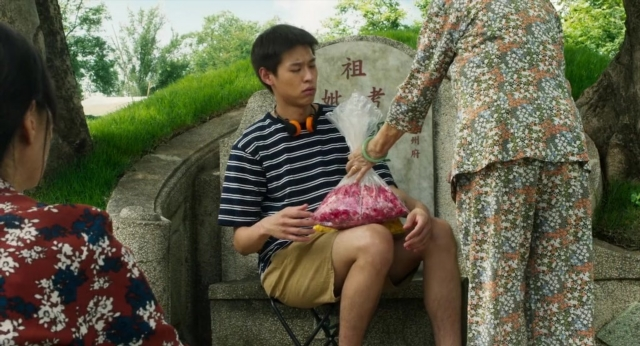 Wide shot frame from Lahn Mah — sitting, standing, food