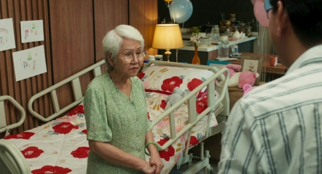 Wide shot frame from Lahn Mah — standing, bed, bottle