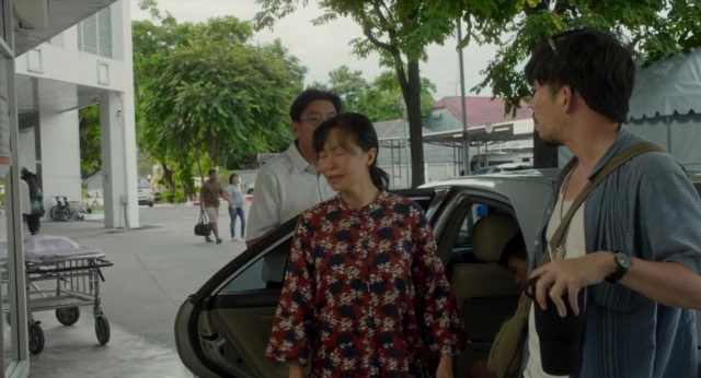 Wide shot frame from Lahn Mah — standing, dialogue, street