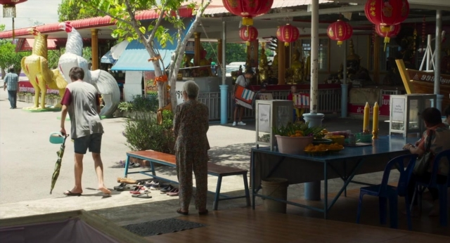 Wide shot frame from Lahn Mah — table, street, dress