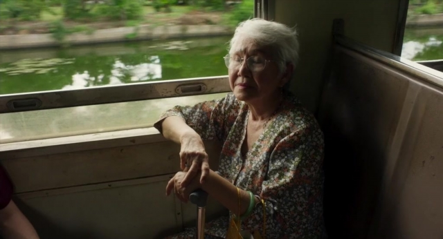 Frame from Lahn Mah — sitting, hand, train