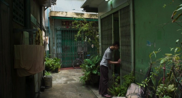 Wide shot frame from Lahn Mah — standing, door, hand