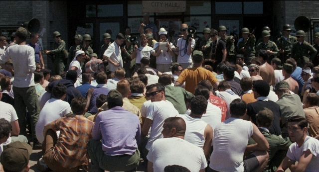 Wide shot frame from Medium Cool — sitting, standing, person