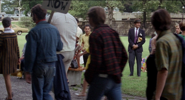 Wide shot frame from Medium Cool — sitting, standing, hat