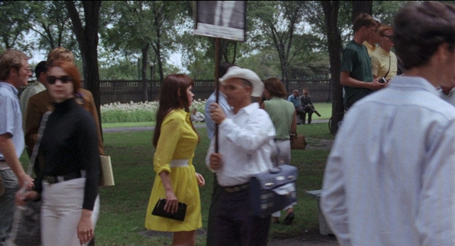 Medium shot frame from Medium Cool — standing, dialogue, hat