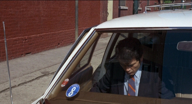 Wide shot frame from Medium Cool — sitting, door, street