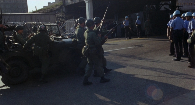 Wide shot frame from Medium Cool — sitting, standing, street