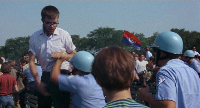 Wide shot frame from Medium Cool — standing, hat, hand