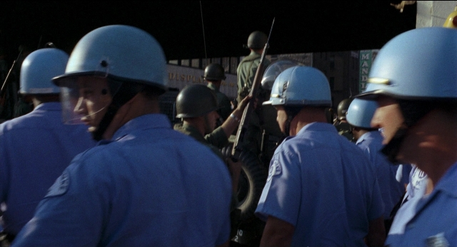 Wide shot frame from Medium Cool — standing, dialogue, hat
