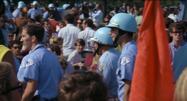 Wide shot frame from Medium Cool — standing, dialogue, hat