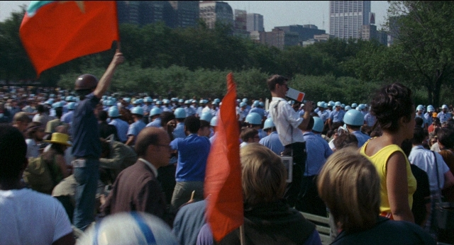 Wide shot frame from Medium Cool — dialogue, flag, person
